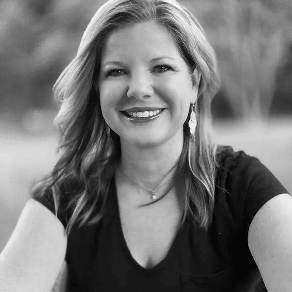 Smiling woman outdoors, wearing earrings and a black shirt.