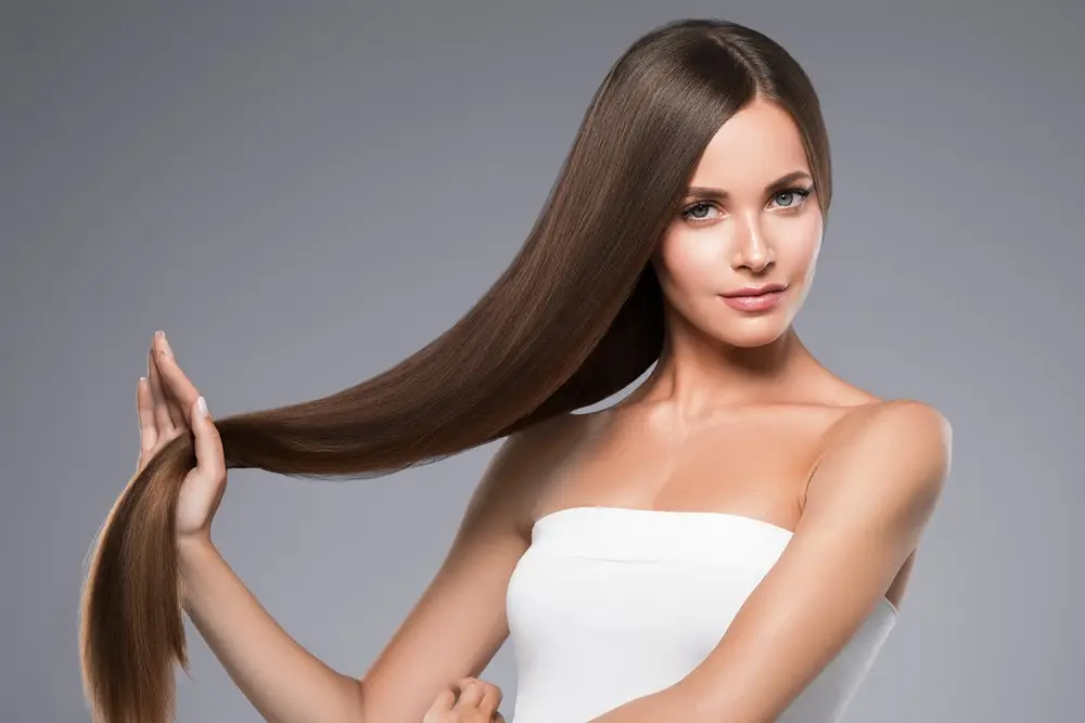 Woman showcasing long, smooth brown hair, wearing a white top.